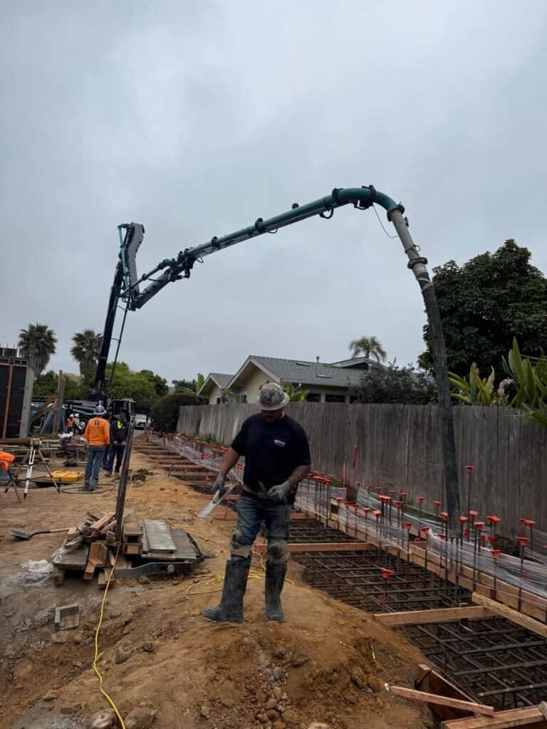 Concrete pouring for foundation construction with concrete pump truck on residential building site.