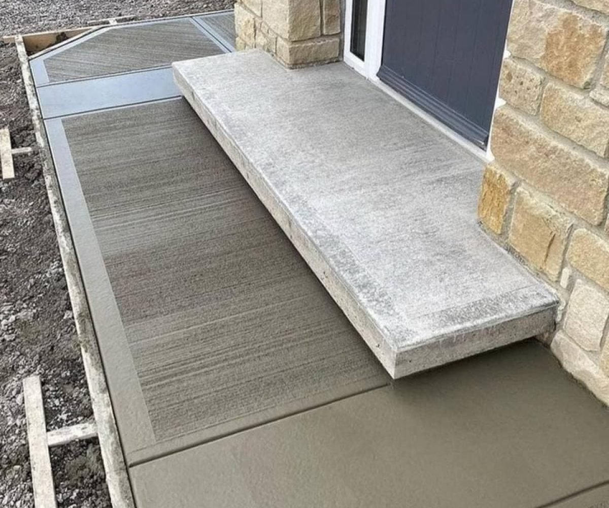 Concrete sidewalk and porch with stamped concrete design near house entrance, showcasing professional concrete services.